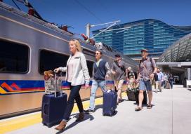 Passengers with suitcases board RTD commuter rail train outside Denver International Airport